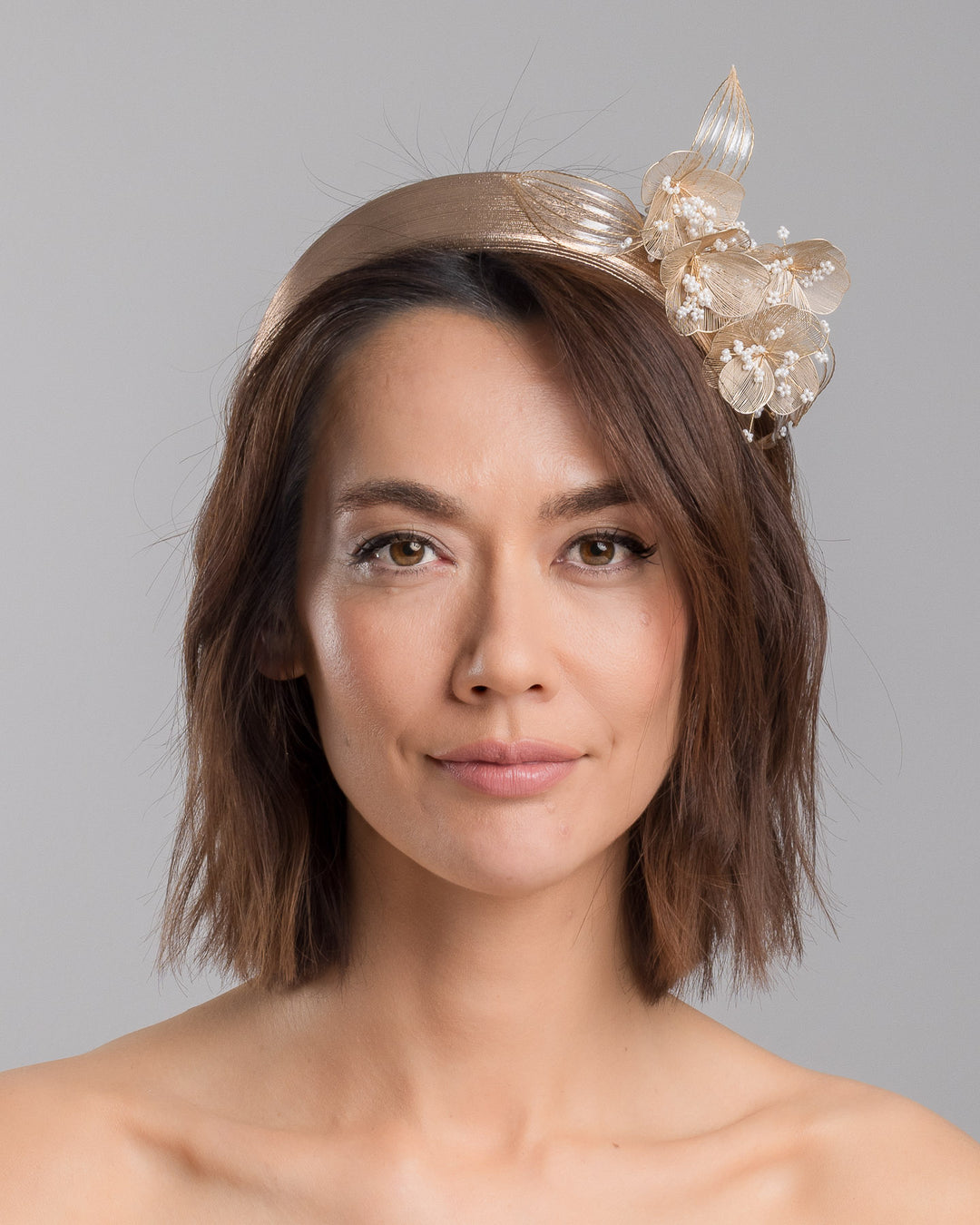 The model is showcasing the front side close up of the gold metallic headband with sculpted floral and leaf embellishments, featuring delicate ivory bead details and an elegant asymmetrical design. Designed and made by Merve Bayindir Millinery.
