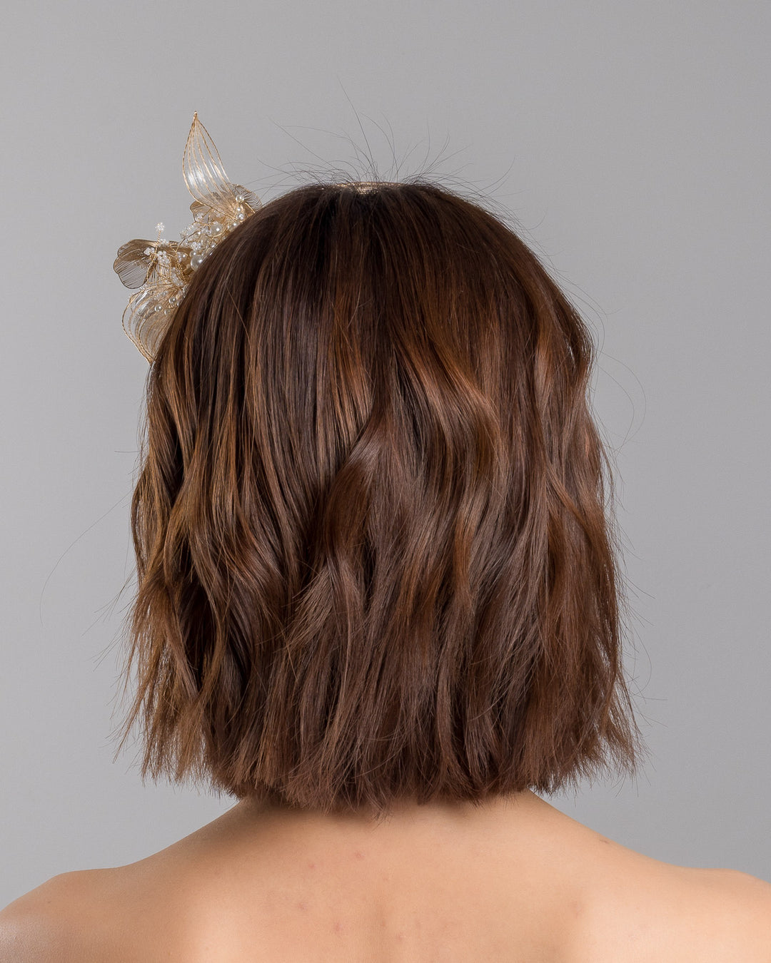 The model is showcasing the back side close up of the gold metallic headband with sculpted floral and leaf embellishments, featuring delicate ivory bead details and an elegant asymmetrical design. Designed and made by Merve Bayindir Millinery.
