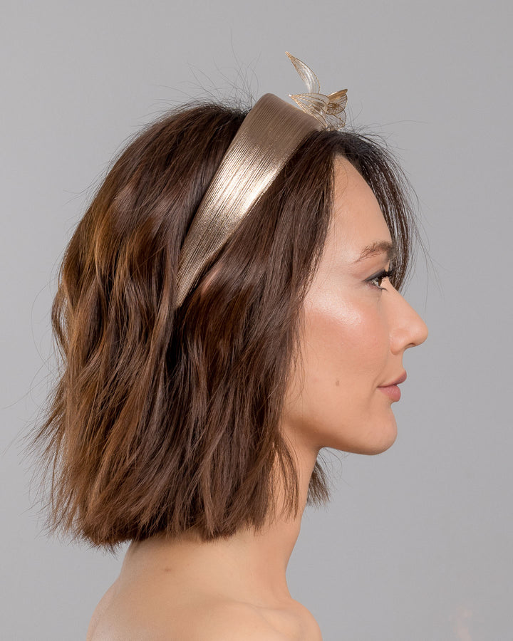 The model is showcasing the right side close up of the gold metallic headband with sculpted floral and leaf embellishments, featuring delicate ivory bead details and an elegant asymmetrical design. Designed and made by Merve Bayindir Millinery.
