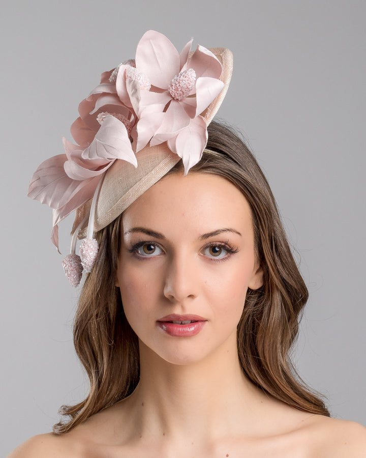 The model is showcasing the front side close up of the blush pink sinamay fascinator adorned with oversized handcrafted satin flowers, beaded centers, sculpted leaves, and curved stem details, mounted on a slim headband. Designed and made by Merve Bayindir Millinery.
