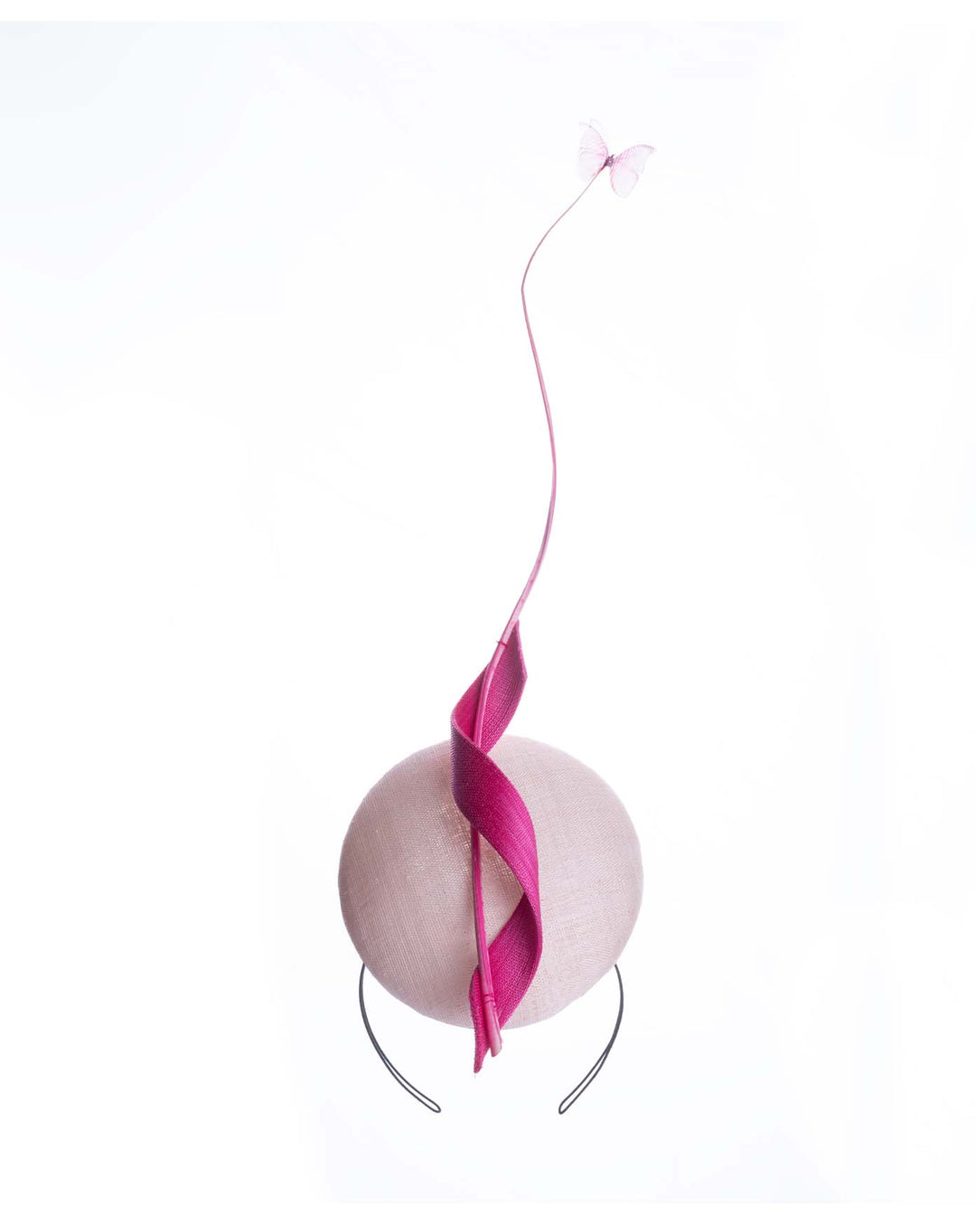 Still life picture of Light pink button shape fascinator attached to a headband. The fascinator is decorated with hot pink jinsin swirl integrated with a pink swirl of ostrich quill in the center. At the tip of the quill swirl there is a pink organza butterfly.