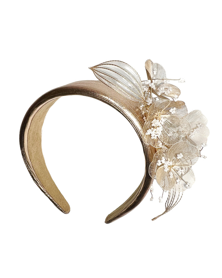 Gold metallic headband with sculpted floral and leaf embellishments, featuring delicate ivory bead details and an elegant asymmetrical design. Designed and made by Merve Bayindir Millinery.

