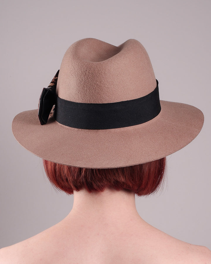 The model is showcasing the back of the Amelie, a classic fedora hat featuring a feathered bow detail; it&