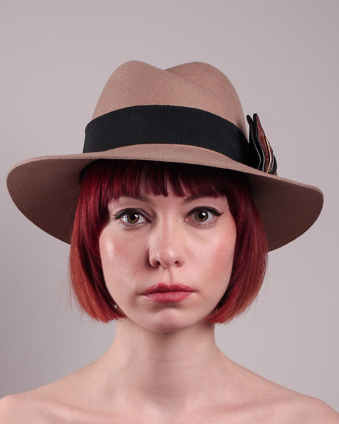 The model is showcasing the front close up of the Amelie, a classic fedora hat featuring a feathered bow detail; it&