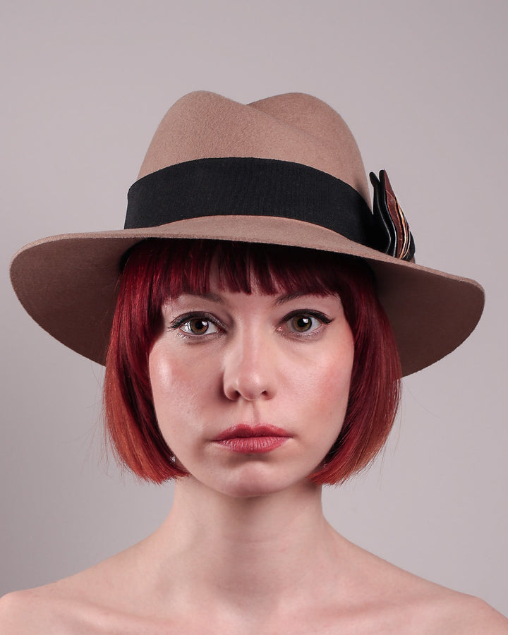 The model is showcasing the front close up of the Amelie, a classic fedora hat featuring a feathered bow detail; it&