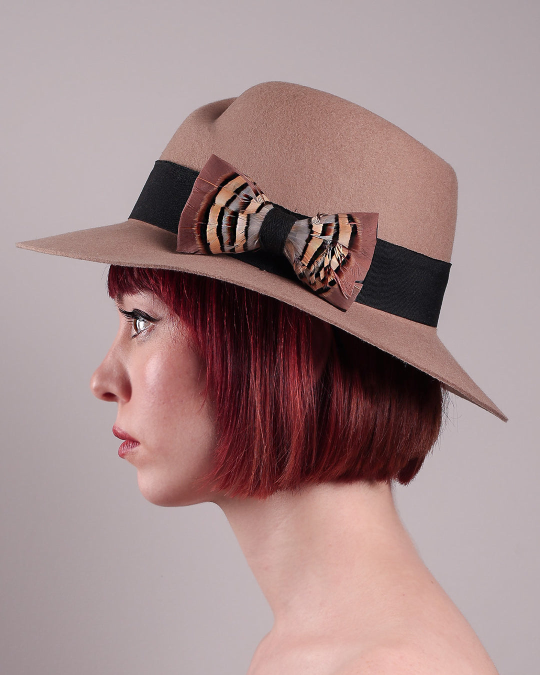 The model is showcasing the left side close up of the Amelie, a classic fedora hat featuring a feathered bow detail; it&
