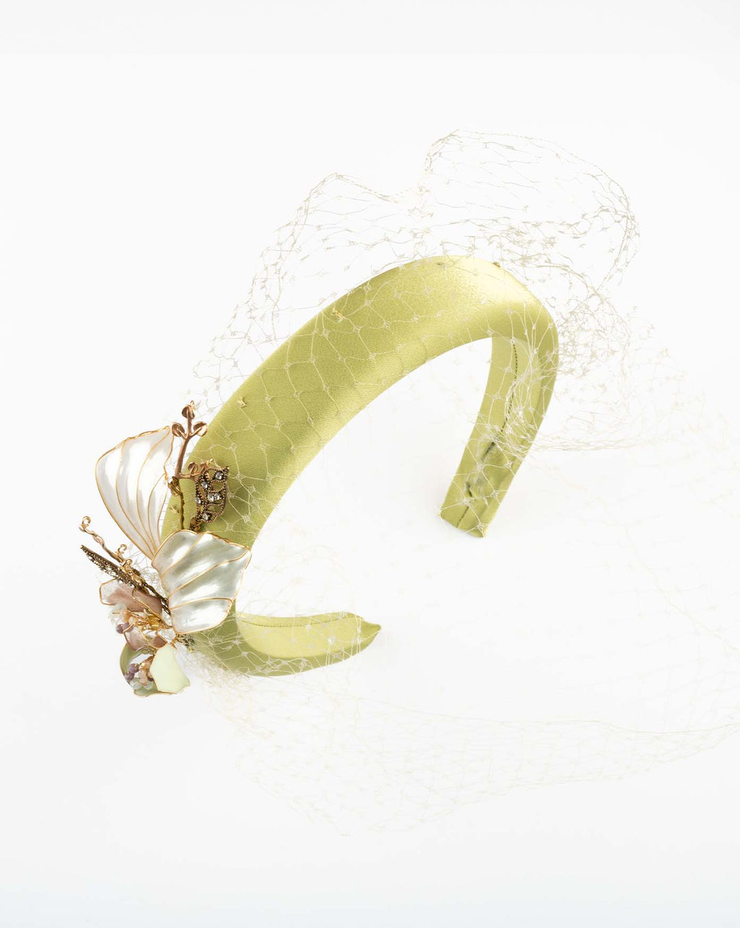 A sheen green silk sateen headband decorated with vintage-looking copper-coloured metal leaves and resin flowers on one side. The front and the top of the headband is finished with sheen green veiling. Made by Merve Bayindir Millinery.