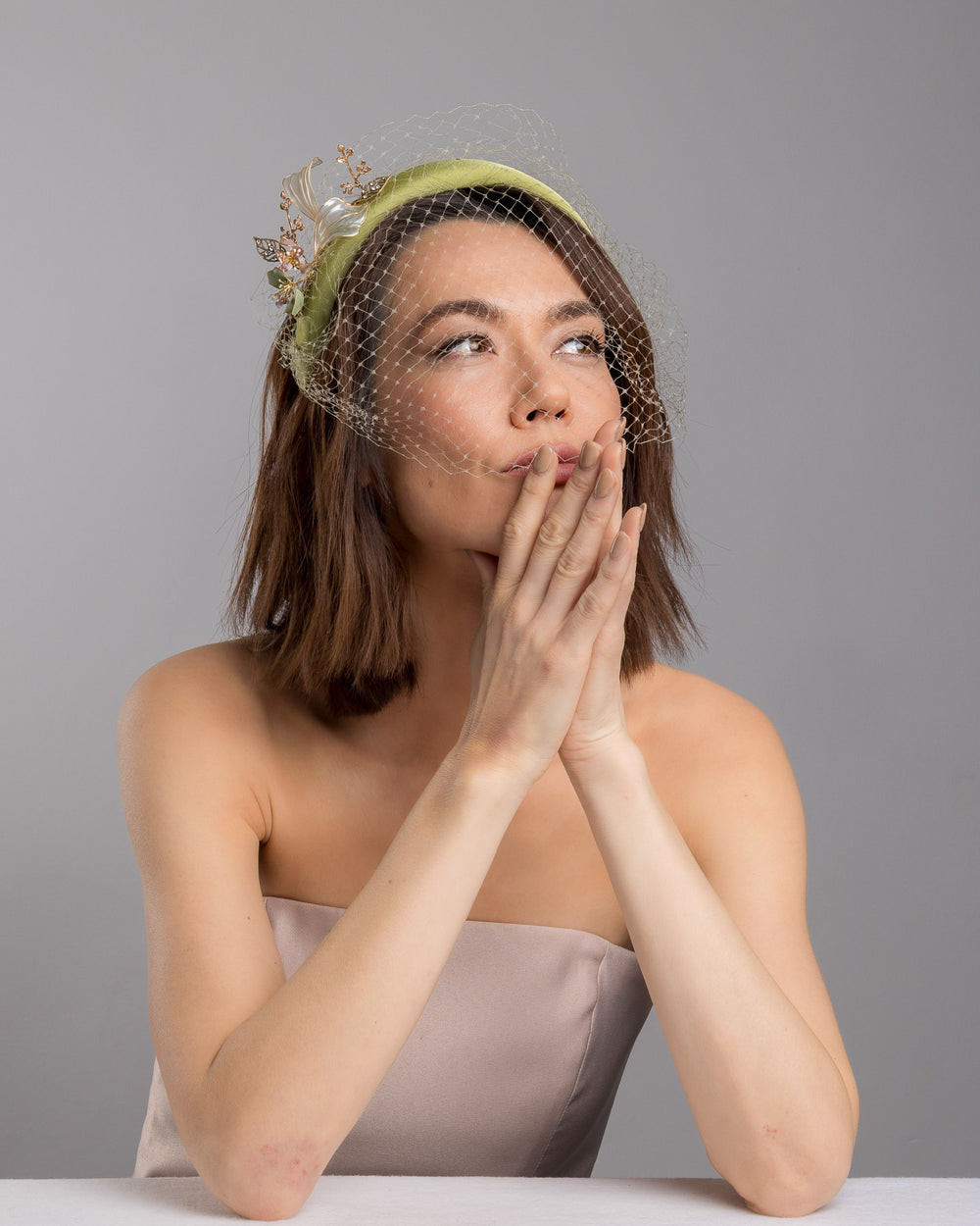 Model is posing wearing Amenita Headband , a sheen green silk sateen headband decorated with vintage-looking copper-coloured metal leaves and resin flowers on one side. The front and the top of the headband is finished with sheen green veiling. Made by Merve Bayindir Millinery.