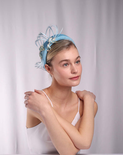 The model is wearing a luxury aqua blue high headband embellished with crystals and decorated with two blue metal birds with trimmed feather tails. 