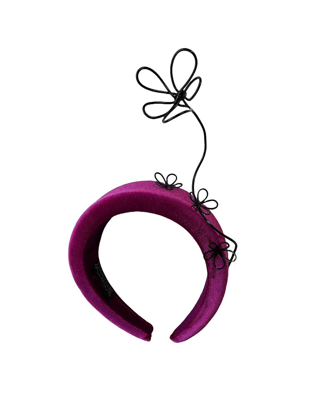 Still life picture of a magenta base, features the Arcana high-formed headband, which sits neatly against the head. At the same time, the matte black floral wire detail ascends upward, accompanied by black wire flowers that create a doodle-like illusion. Designed by Merve Bayindir