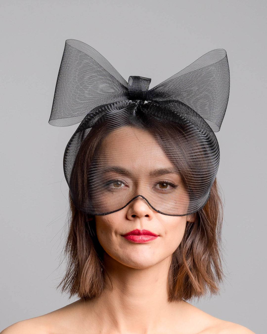 Model is showcasing the rfront of the black mesh cage-style constructed Astrea mask. On top of the cage-style mesh mask, there is a mesh bow. The mask is fitted with a thin headband. The mask is perfect for high-fashion events or special parties. Made by Merve Bayindir Millinery.