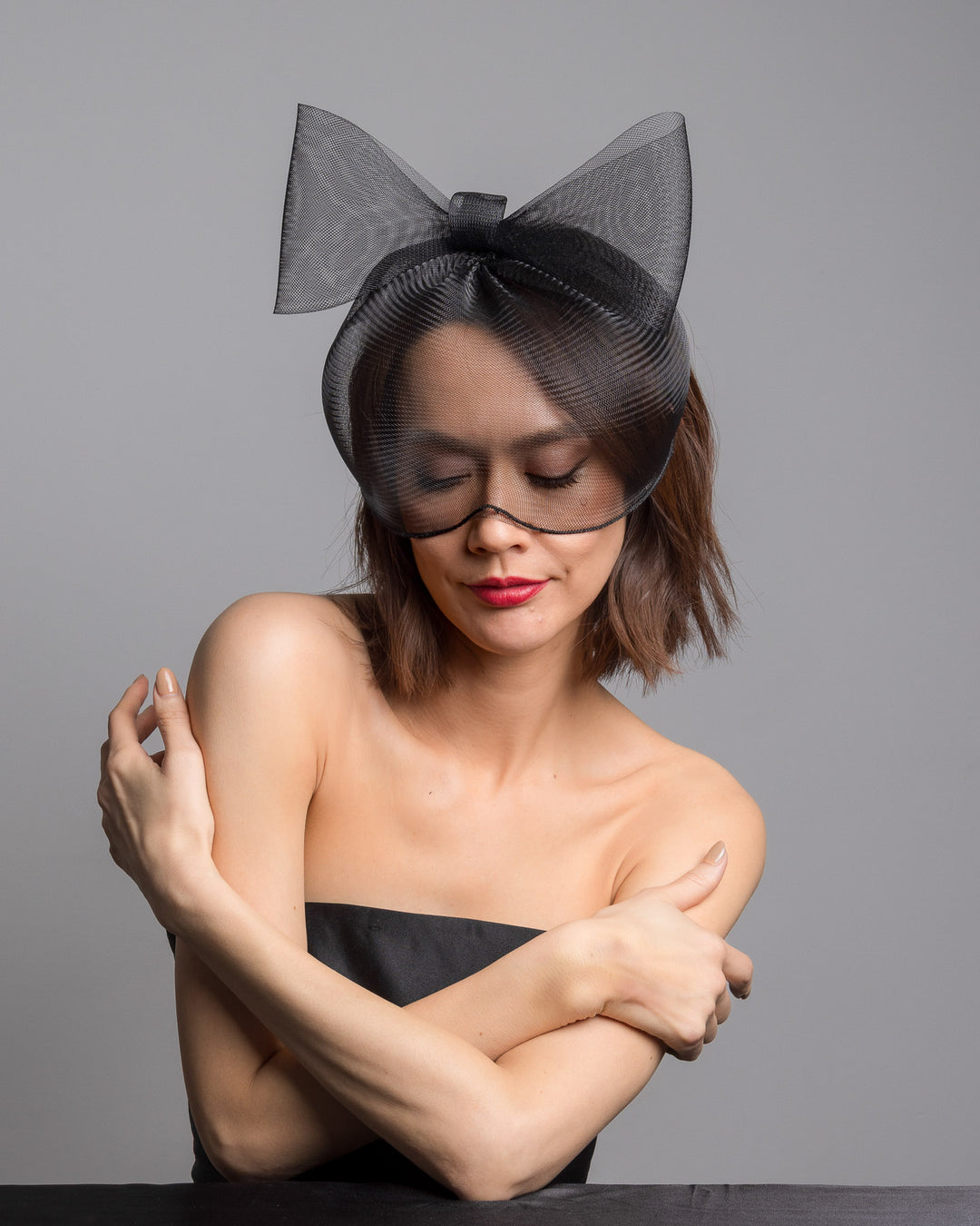 Model is posing wearing the black mesh cage-style constructed Astrea mask. On top of the cage-style mesh mask, there is a mesh bow. The mask is fitted with a thin headband. The mask is perfect for high-fashion events or special parties. Made by Merve Bayindir Millinery.