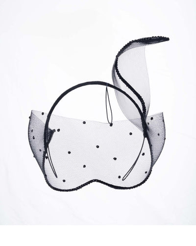 The black mesh headpiece is adorned with small black crystals. It features a design with a prominent bow-like structure on one side embellished with black crystals. The delicate mesh has a wire band to be fitted to the head.