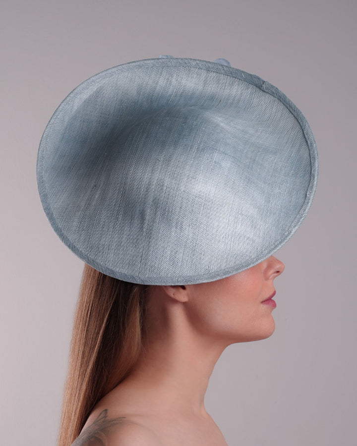 Model is showcasing the right side of the blue saucer hat with an high angle decorated with blue silk flowers in the left high inner side, the hat is fitted on a mini saucer that is secured to the head with &amp;nbsp;a wire headband and elastic as well as a comb.