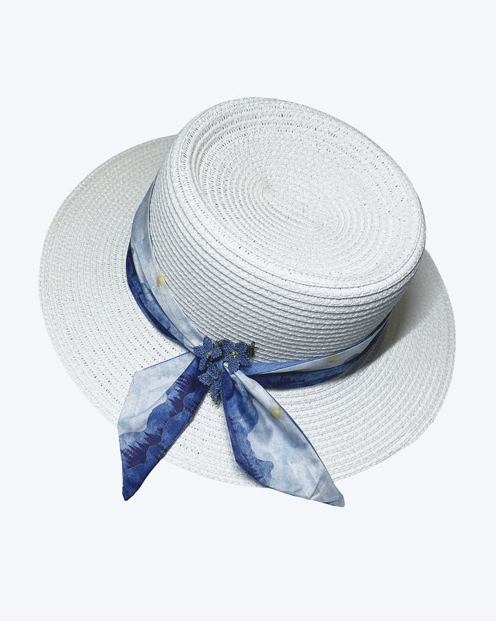 White woven straw boater hat with a wide brim, wrapped in a soft blue watercolour scarf and finished with delicate blue beaded floral embellishments at the side. Designed by Merve Bayindir millinery.