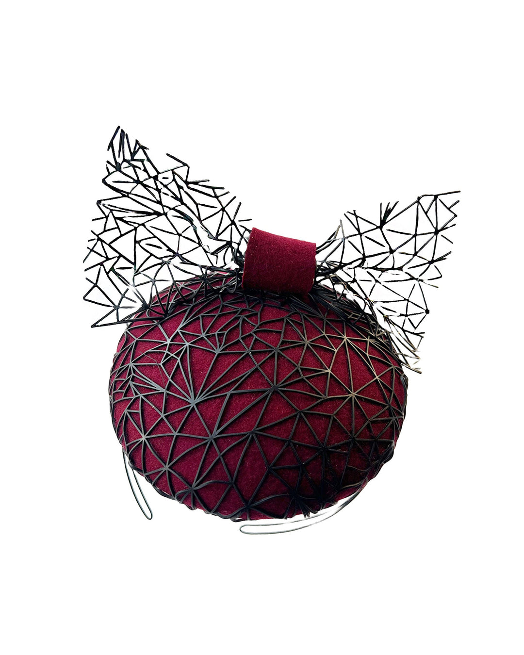 Still life picture of Bijou, featuring a handcrafted raffia fascinator in rich burgundy felt, with button shape. Its structured base is overlaid with an angular black netting design and crowned with an architectural bow that fuses avant-garde with elegance. Designed by Merve Bayindir.
