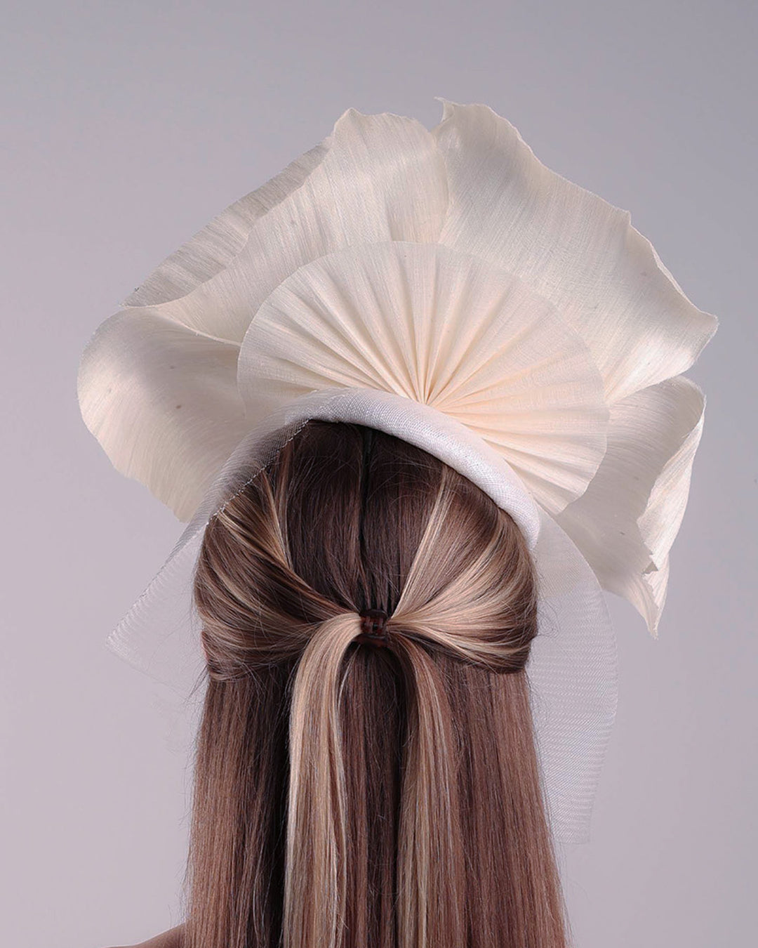 Model is showcasing the back of a large white hand made silk abaca flower, decorated with silver crystals, placed one a button shaped white sinamay fascinator from the left side A white crinoline veil is placed between the hat and the flower to cover the face. The button base is fixed on a custom headband and secured with an additional elastic.