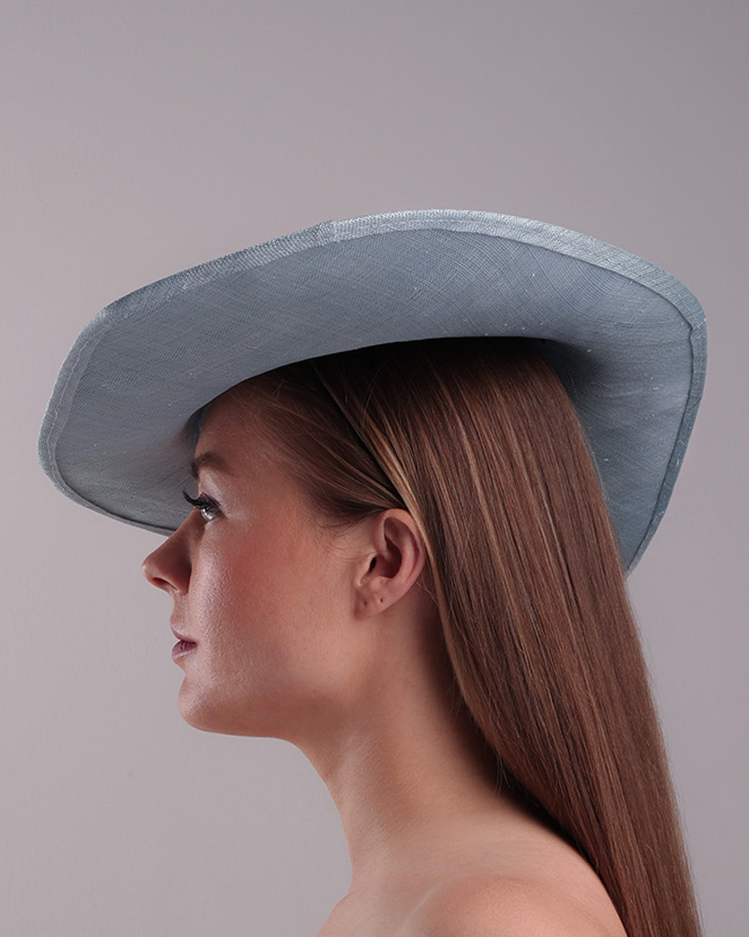 The model is showcasing the left side of a blue asymetric whide brim hat, tilted to the right, decorated with pressed natural flowers creatinga almost 3D dimensional print affect on the hat. Fitted with a wired headband and additionally secured with elastic.
