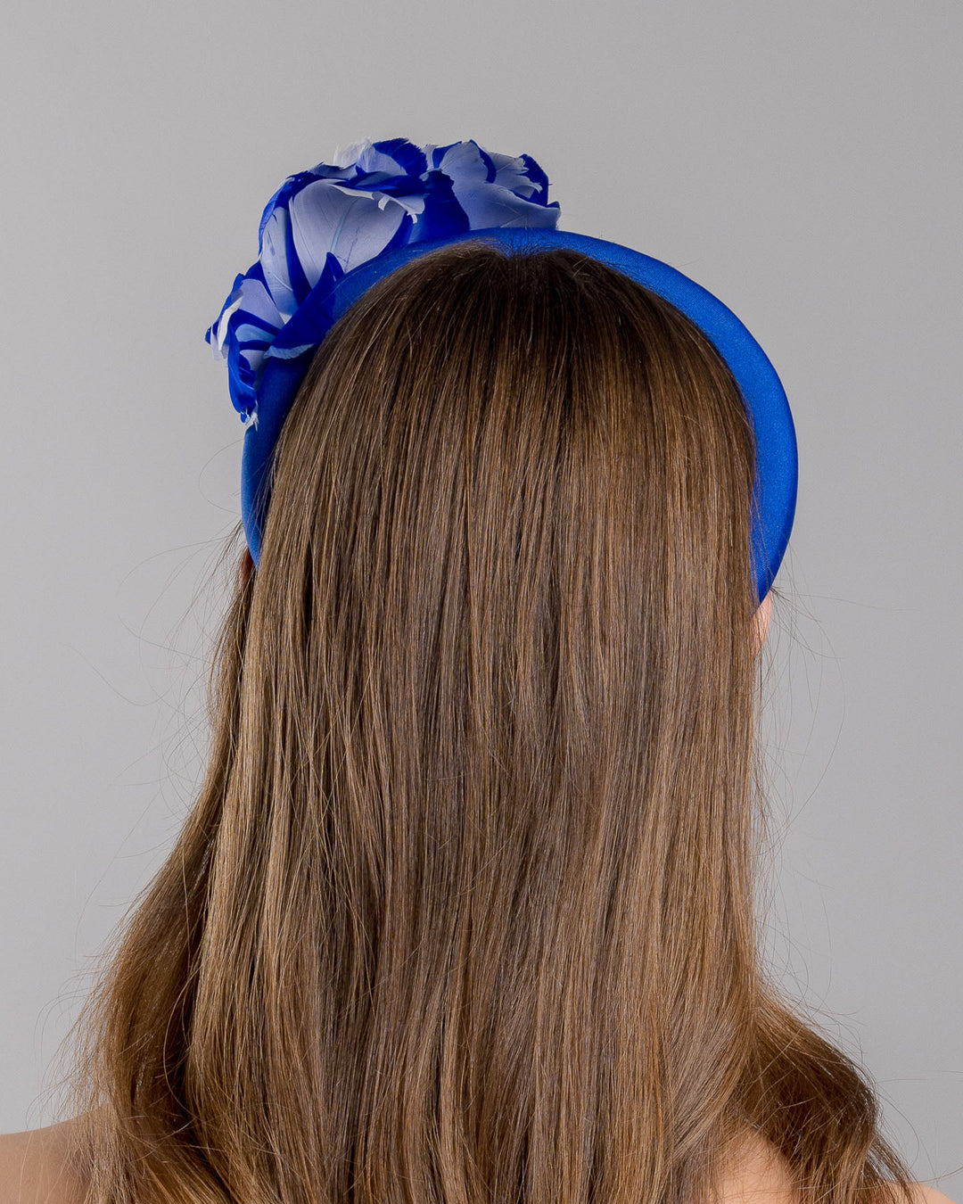 Model is showcasing the left side close up of cobalt blue high headband showcases a metal koi fish decorated with blue shades of crystals adorned with feathers behind it to create the illusion of a wave. The luxury headband is a contemporary statement. Made by Merve Bayindir Millinery.