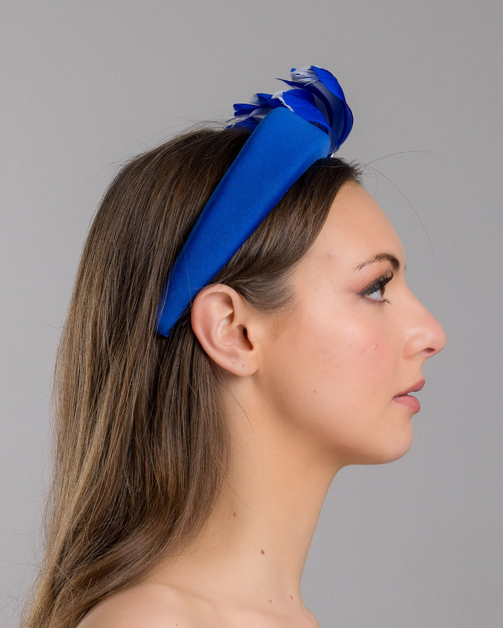 Model is showcasing the right side close up of cobalt blue high headband showcases a metal koi fish decorated with blue shades of crystals adorned with feathers behind it to create the illusion of a wave. The luxury headband is a contemporary statement. Made by Merve Bayindir Millinery.