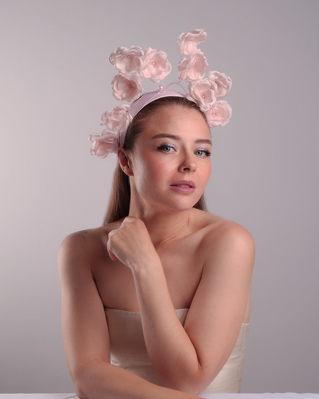 Model is showcasing the front right side of a flat pink silk sateen headband decorated with pink wire branches embellished with medium pink roses centred with plastic pink pearls.