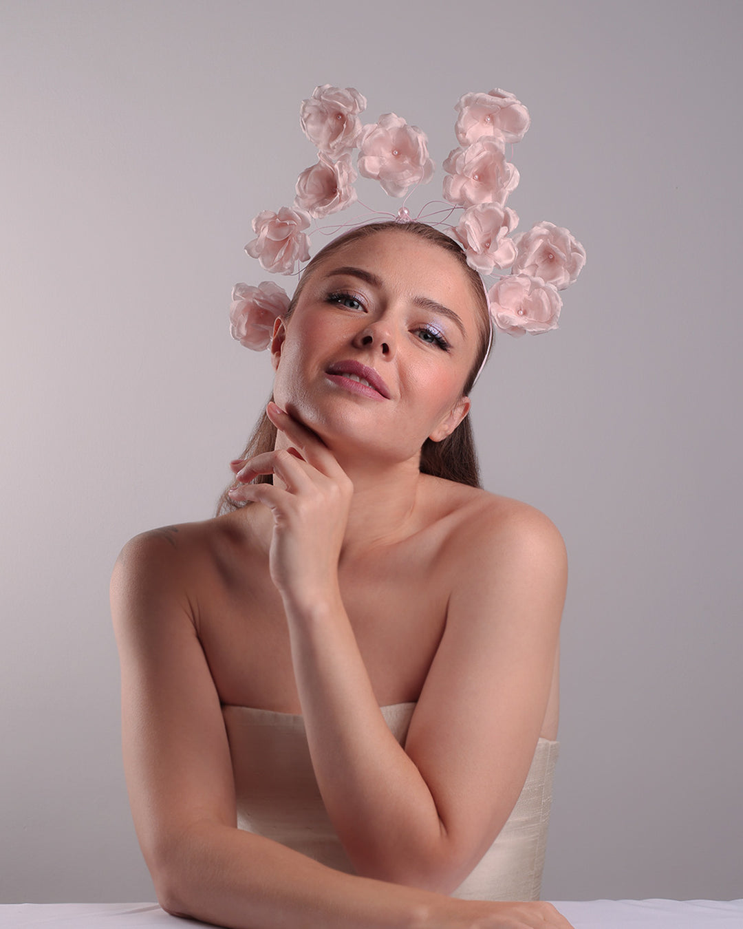 Model is showcasing the front of a flat pink silk sateen headband decorated with pink wire branches embellished with medium pink roses centred with plastic pink pearls.