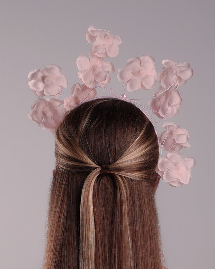 Model is showcasing the back of a flat pink silk sateen headband decorated with pink wire branches embellished with medium pink roses centred with plastic pink pearls.