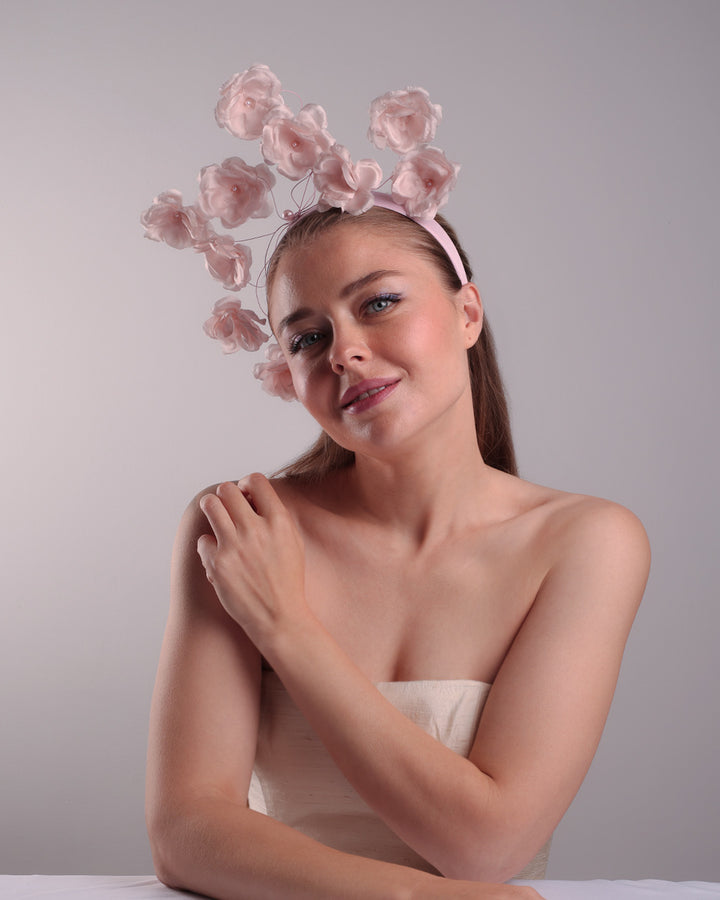 Model is showcasing the front left side of a flat pink silk sateen headband decorated with pink wire branches embellished with medium pink roses centred with plastic pink pearls.