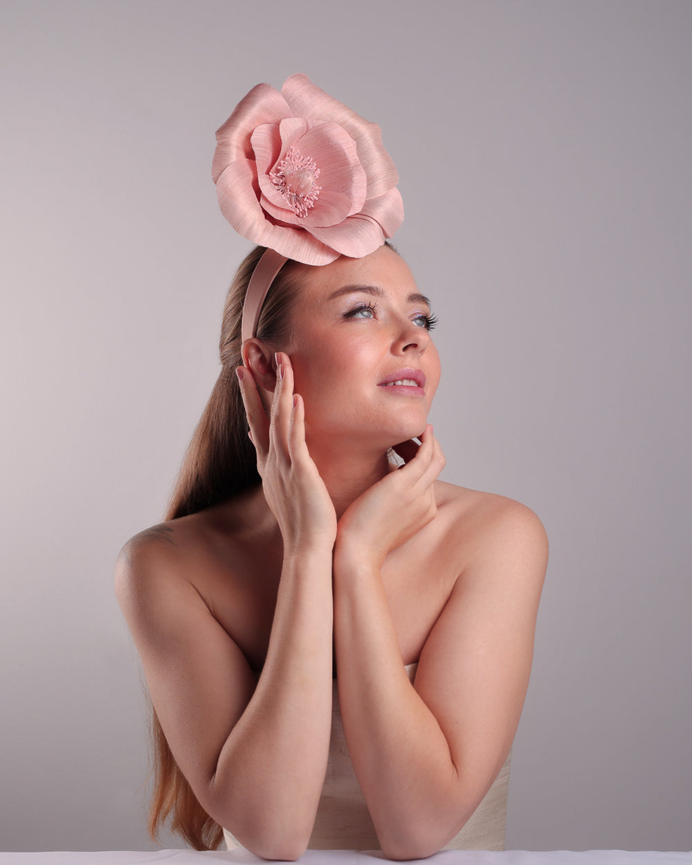 Model is showcasing the lower  front right angle of a medium light pink silk abaca flower fitted on the right centre of a flat pink silk headband towards the right side of flat silk headband.