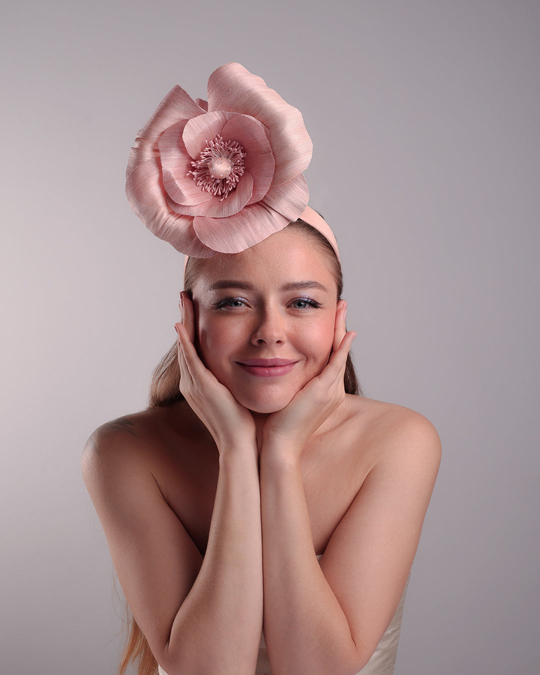 Model is showcasing the front of a medium light pink silk abaca flower fitted on the right centre of a flat pink silk headband towards the right side of flat silk headband.