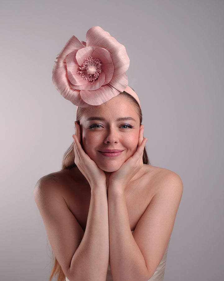 Model is showcasing the front of a medium light pink silk abaca flower fitted on the right centre of a flat pink silk headband towards the right side of flat silk headband.