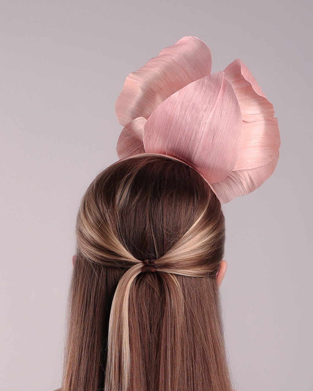 Model is showcasing the back a medium light pink silk abaca flower fitted on the right centre of a flat pink silk headband towards the right side of flat silk headband.