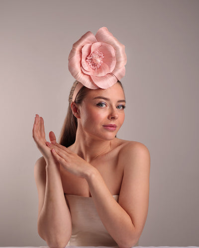 Model is showcasing the front right angle of a medium light pink silk abaca flower fitted on the right centre of a flat pink silk headband towards the right side of flat silk headband.