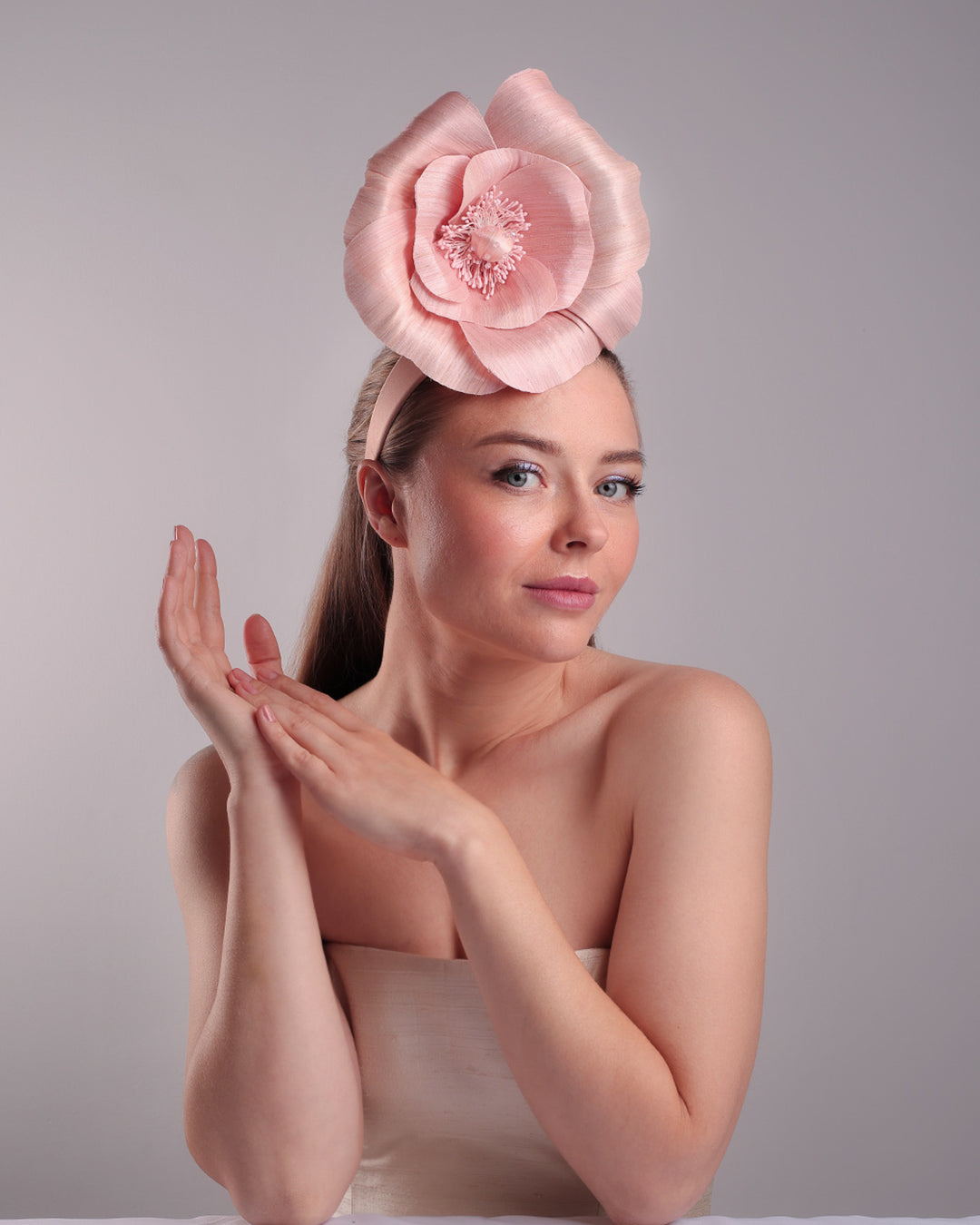Model is showcasing the front right angle of a medium light pink silk abaca flower fitted on the right centre of a flat pink silk headband towards the right side of flat silk headband.