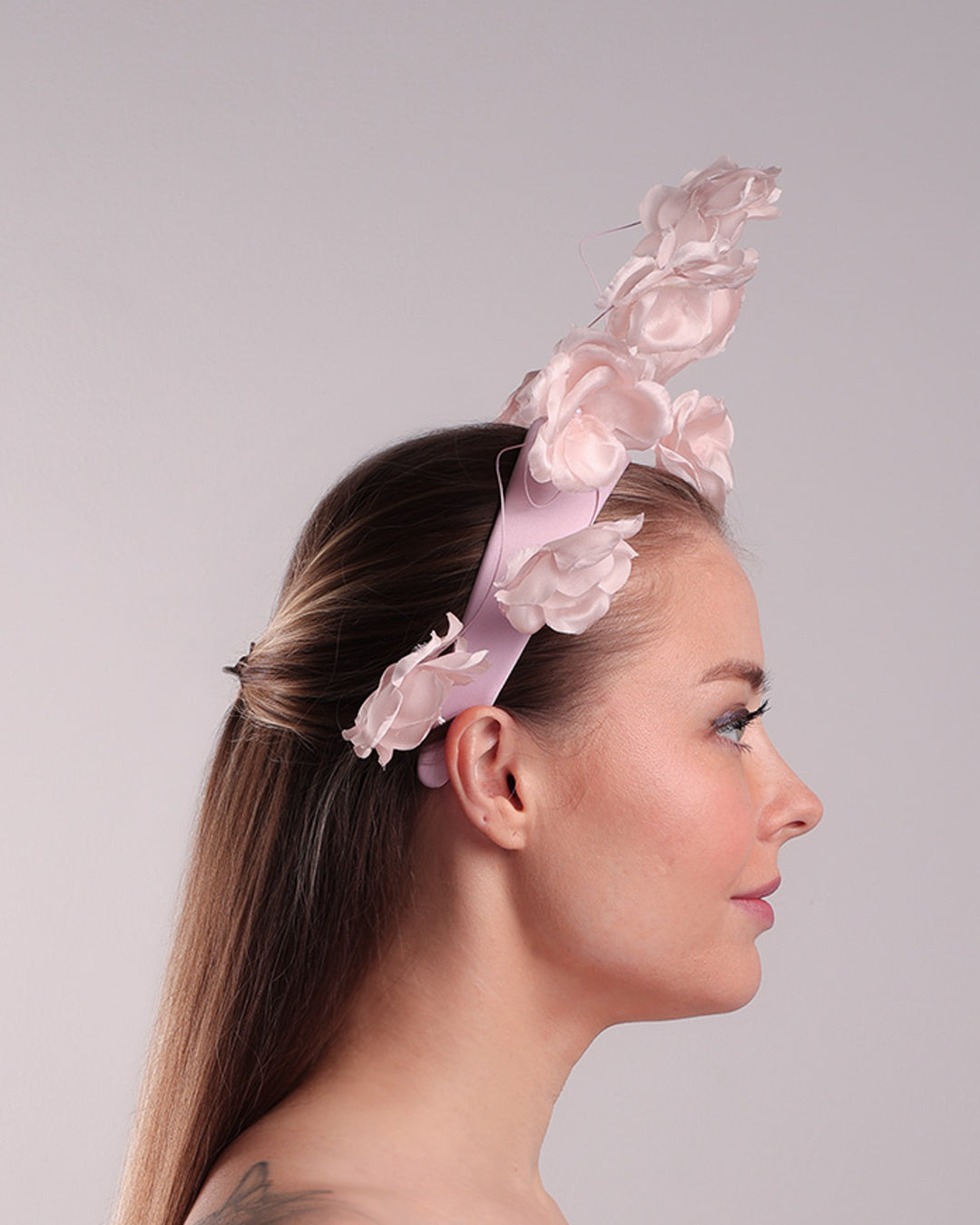 Model is showcasing the right side of a flat pink silk sateen headband decorated with pink wire branches embellished with medium pink roses centred with plastic pink pearls.