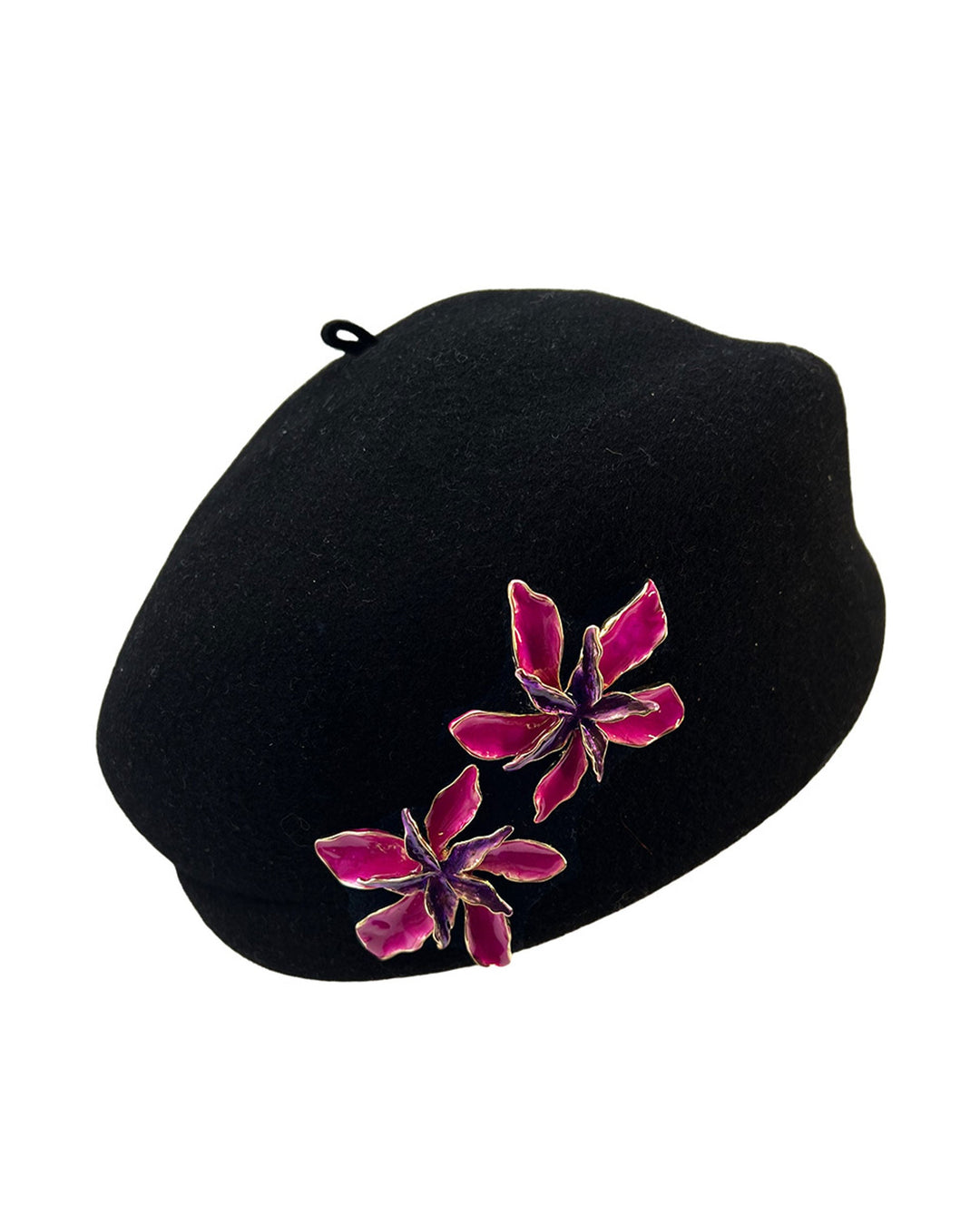 The still life picture of the black wool beret hat is decorated with metal, two bold floral embellishments in vivid fuchsia. The side beret is higher on the left side and shorter on the right side, with a bit of felt ribbon detail on the top centre. Designed by Merve Bayindir.