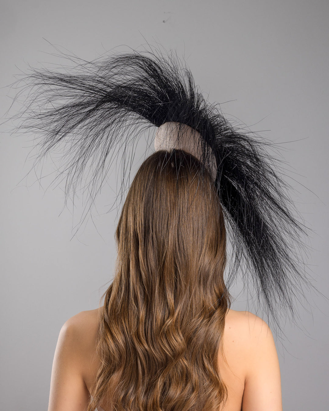 The model is showcasing the back side close up of the pink button-shaped fascinator adorned with strikingly long, burnt-black peacock feathers radiating outward, embellished with a handmade black rose. Designed and made by Merve Bayindir Millinery.
