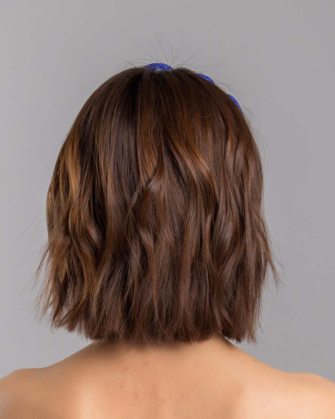 The model is showcasing the back side close up of the light silver headband with a faux leather base, wrapped in bold looping cobalt blue crystal-embellished cords, creating a sculptural, high-shine statement design. Designed and made by Merve Bayindir Millinery.
