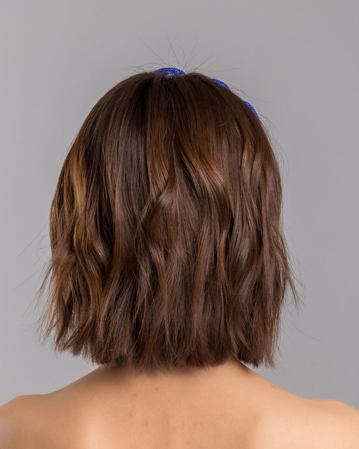 The model is showcasing the back side close up of the light silver headband with a faux leather base, wrapped in bold looping cobalt blue crystal-embellished cords, creating a sculptural, high-shine statement design. Designed and made by Merve Bayindir Millinery.
