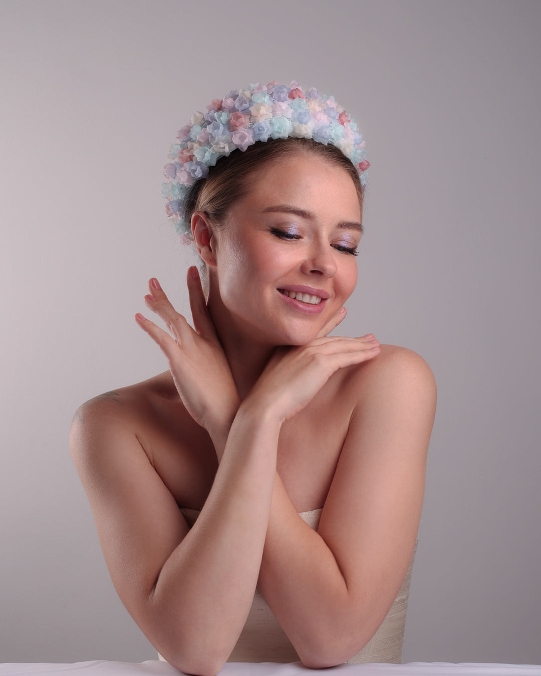 The model is presenting the right front angle of a blue pillbox style hat, embellished with multi colour silk organza flowers.