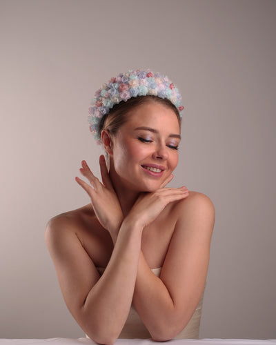 The model is presenting the right front angle of a blue pillbox style hat, embellished with multi colour silk organza flowers.