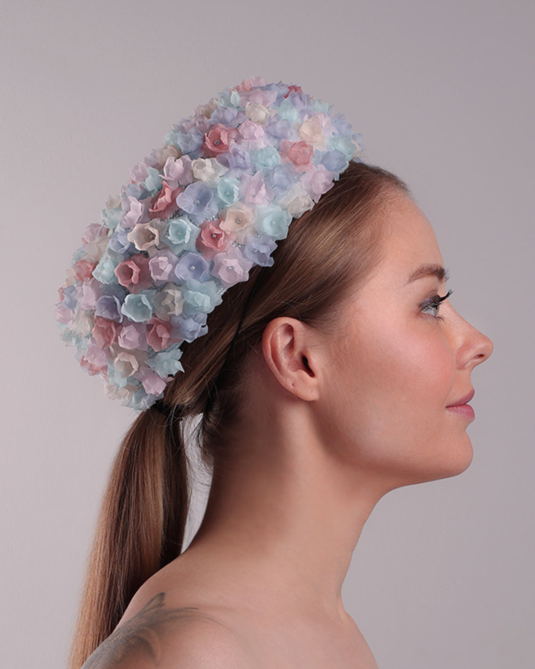 The model is presenting the right side of the blue pillbox style hat, embellished with multi colour silk organza flowers.