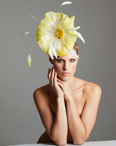 The picture featuring a large, vibrant yellow flower design fascinator is crafted with delicate yellow petals that fan out from the centre, complemented by wispy yellow feathers