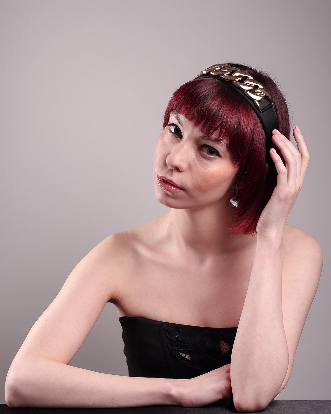 The model showcases the front from the left angle of the Celeste Headband, handcrafted from a satin black Alice headband and crowned with a statement gold chain. Designed by Merve Bayindir.