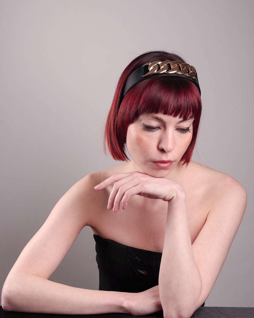 The model showcases the front right angle of the Celeste Headband, handcrafted from a satin black Alice headband and crowned with a statement gold chain. Designed by Merve Bayindir.