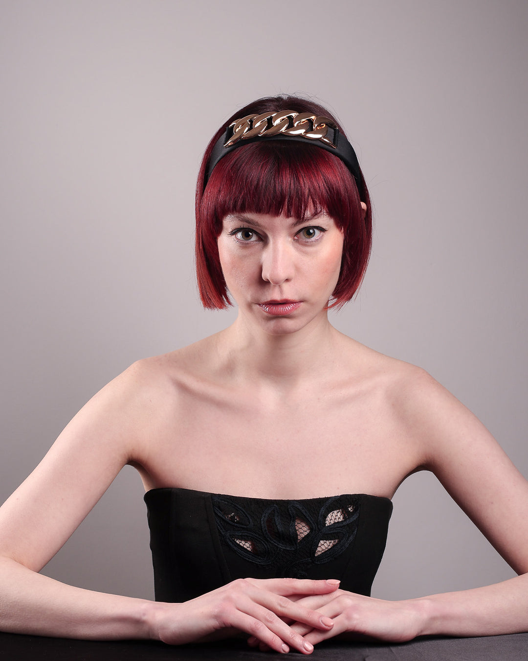 The model showcases the front of the Celeste Headband, handcrafted from a satin black Alice headband and crowned with a statement gold chain. Designed by Merve Bayindir.