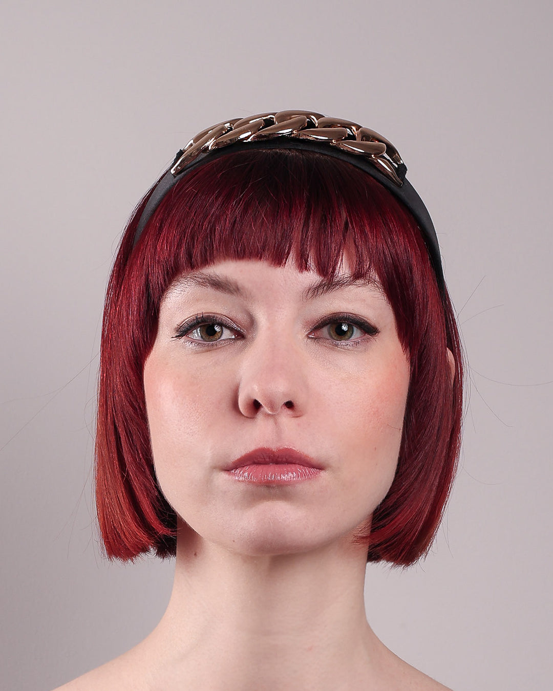 The model showcases the front close up of the Celeste Headband, handcrafted from a satin black Alice headband and crowned with a statement gold chain. Designed by Merve Bayindir.