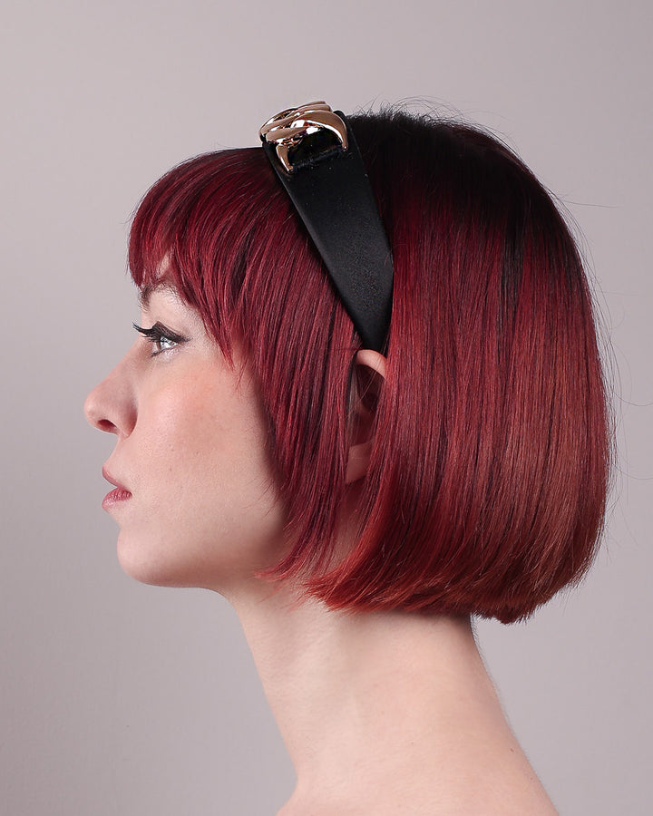 The model showcases the left side close up of the Celeste Headband, handcrafted from a satin black Alice headband and crowned with a statement gold chain. Designed by Merve Bayindir.