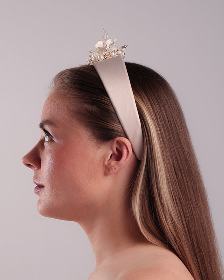 The model is showcasing the left side of an Alice style flat silk headband decorated with ivory resin flower arrangment with beads.