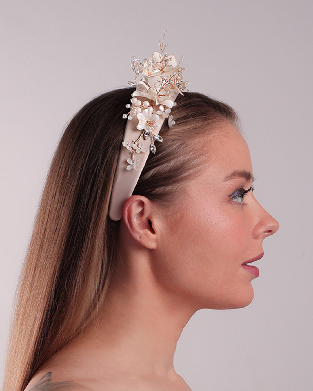 The model is showcasing the right side of an Alice style flat silk headband decorated with ivory resin flower arrangment with beads.